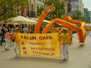 Praktykujący Falun Dafa niosą transparent, na którym zostały zapisane trzy główne zasady praktyki przy użyciu chińskich znaków i w tłumaczeniu na język polski. Za niosącymi transparent tańczący Złoty Smok, parada Falun Dafa, Łódź, 27.07.2024 r. (fot. dzięki uprzejmości Marka Sybilaka)