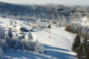 Ksiądz z parafii luterańskiej w Szczyrku zbiera narty carvingowe, szczególnie dziecięce, snowboardy, kijki i buty, używane, lecz w dobrym stanie. Ofiarowuje je tym, których nie stać na zakup, a chcą jeździć. Zdjęcie ilustracyjne (<a href="https://unsplash.com/@maxc4?utm_content=creditCopyText&amp;utm_medium=referral&amp;utm_source=unsplash">Max Cyprys</a> / <a href="https://unsplash.com/photos/an-aerial-view-of-a-ski-resort-surrounded-by-trees-Zq4NNqjkjfE?utm_content=creditCopyText&amp;utm_medium=referral&amp;utm_source=unsplash">Unsplash</a>)